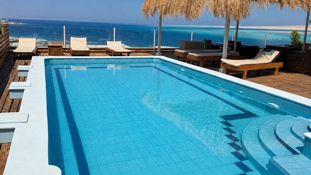 Una piscina amb vistes a l'oceà, gandules i un parasol de palla.