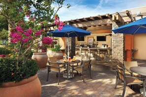 An outdoor patio area with tables and chairs, a bar, and potted plants.