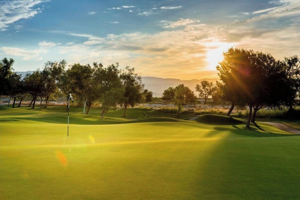 A golf course with a flagstick, trees, and a sunset.