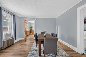 Uma área de jantar moderna com mesa de madeira, cadeiras estofadas cinzas e tapete com padrão azul.