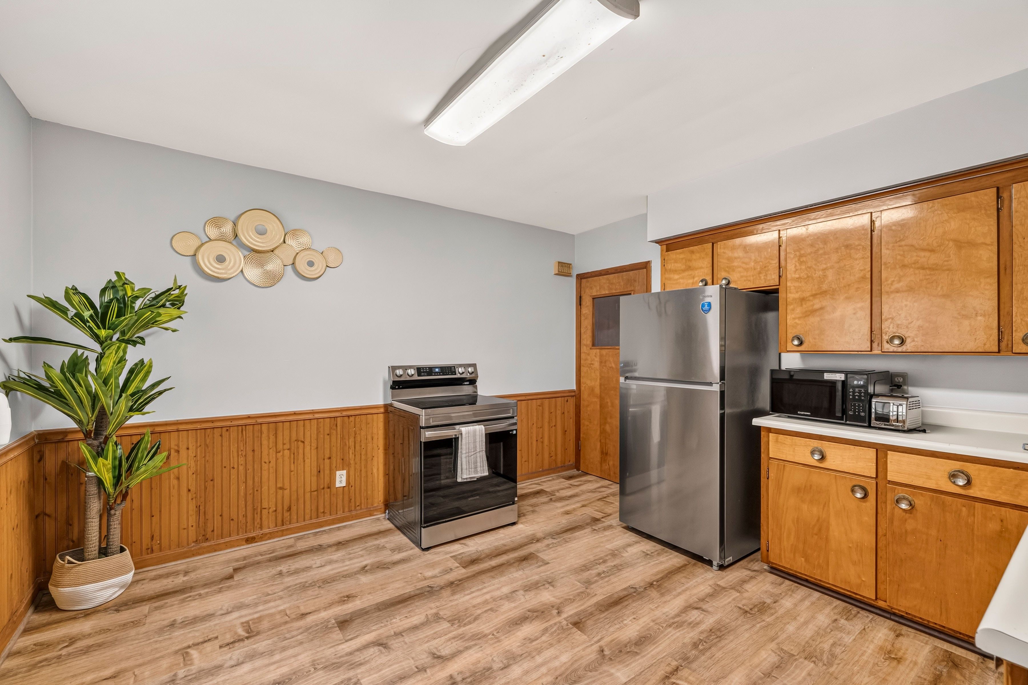 A kitchen with wooden cabinets, a stainless steel refrigerator, a microwave, an oven, and a potted plant.