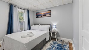 Una camera da letto con un letto, un comodino, una lampada, un quadro e una finestra con tende.