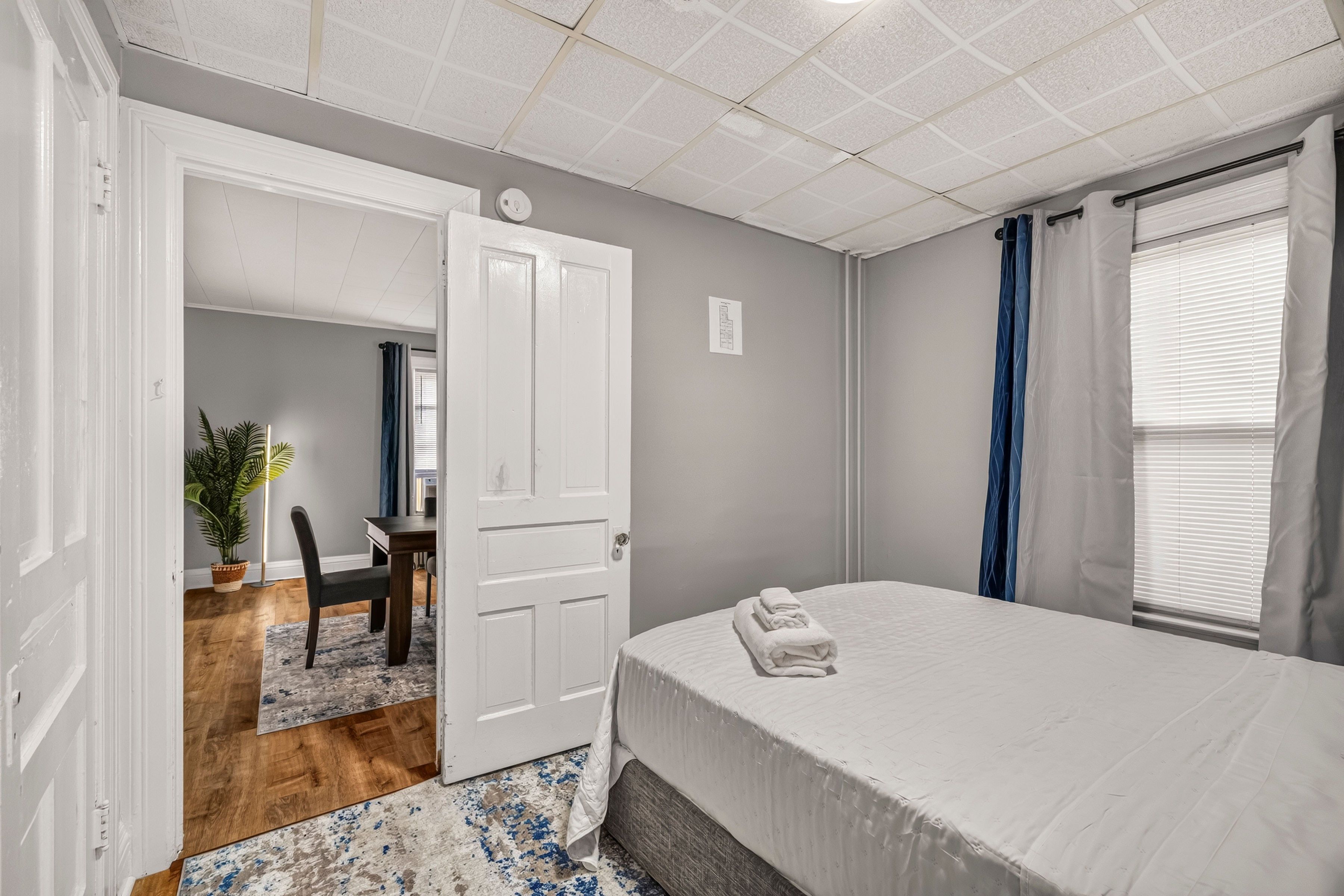Une chambre à coucher avec un lit, un bureau et une chaise. Une porte donne accès à une autre pièce.