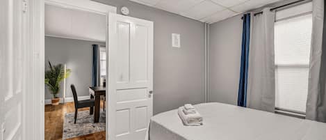 A bedroom with a bed, a desk, and a chair. There is a door leading to another room.