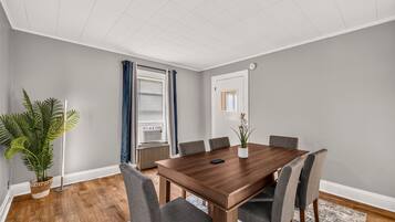 A conference room with a wooden table, grey chairs, a potted plant, and a window with blinds.