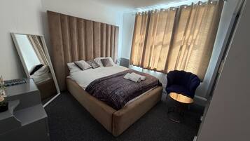 A modern hotel room with a large bed, a bedside table, a chair, and a window with curtains.