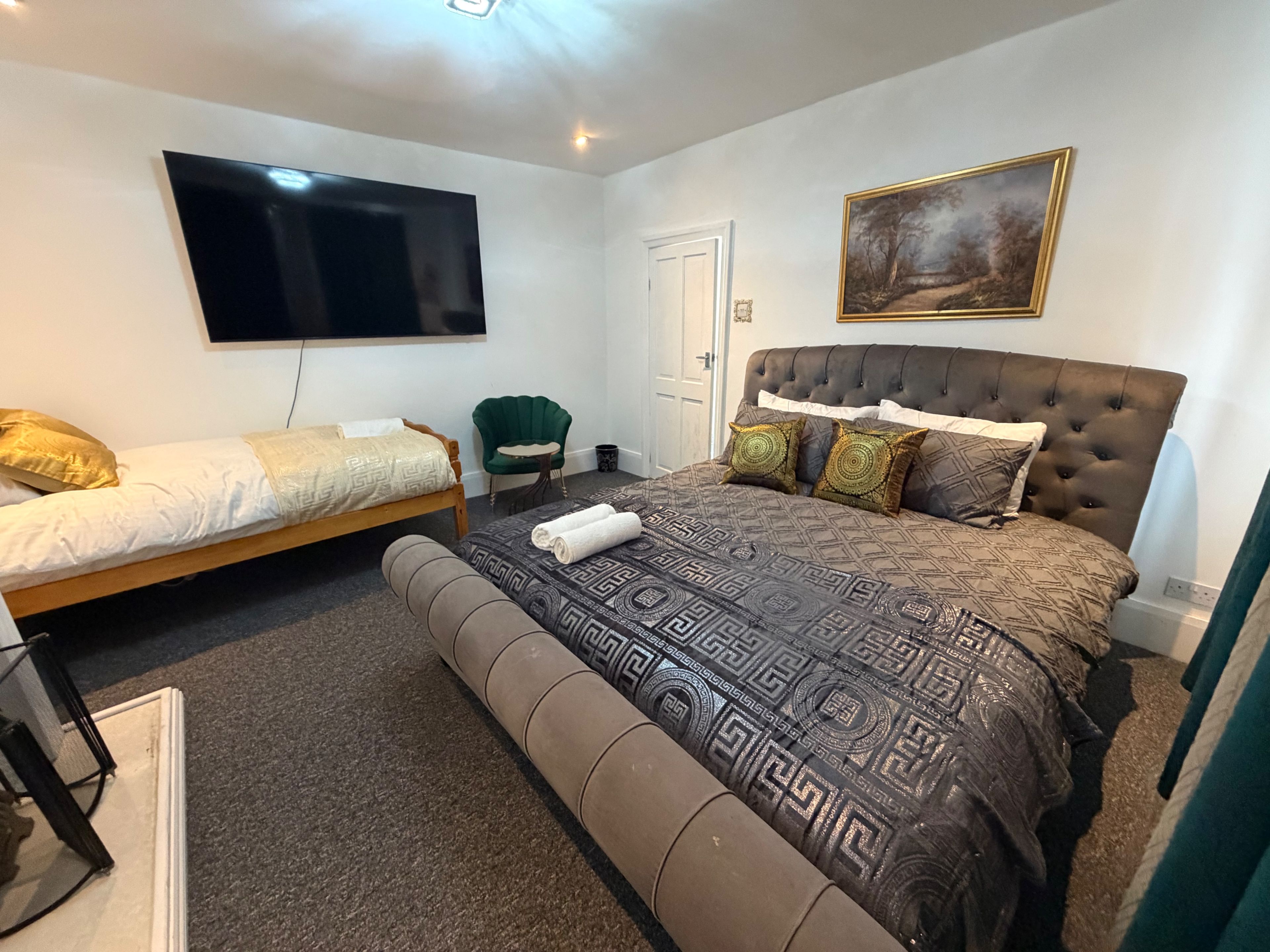 A bedroom with a large bed, a smaller bed, a television, a chair, and a painting on the wall.