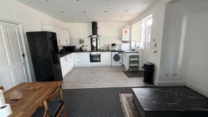 A modern kitchen with white cabinets, a black refrigerator, a microwave, a stove, and a washing machine. - House Sleeps 7 With Parking (Cheadle)