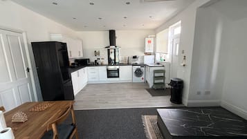 A modern kitchen with white cabinets, a black refrigerator, a microwave, a stove, and a washing machine.