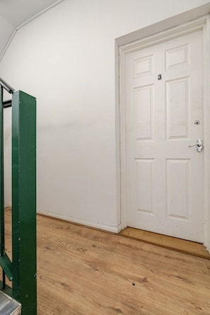 A room with a white door marked with the number 3, a green metal structure, and wooden flooring. - Arsenal Corner Studio, 4 minutes to Kings Cross, with Ensuite & Self Check-In (London)