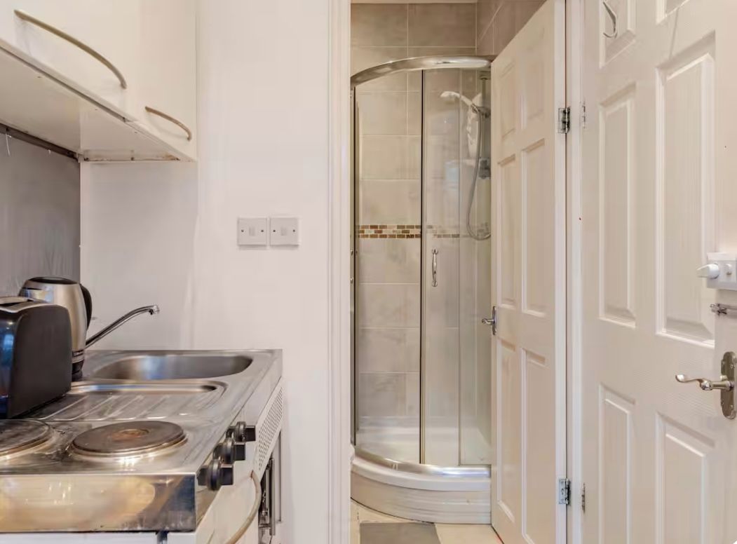 A kitchenette with a stove and sink, a glass shower enclosure, and a white door.