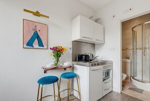 A compact kitchen with a gas stove, oven, and a small bar area with stools. - Arsenal Corner Studio, 4 minutes to Kings Cross, with Ensuite & Self Check-In (London)