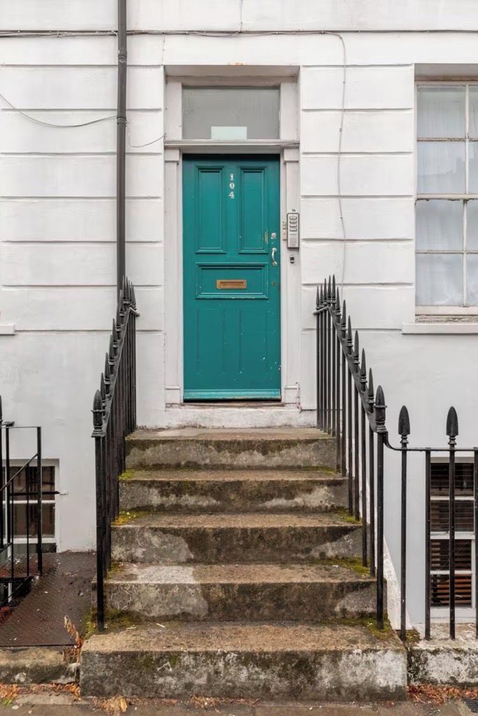 A set of stone steps leading to a teal door with a small window above it.