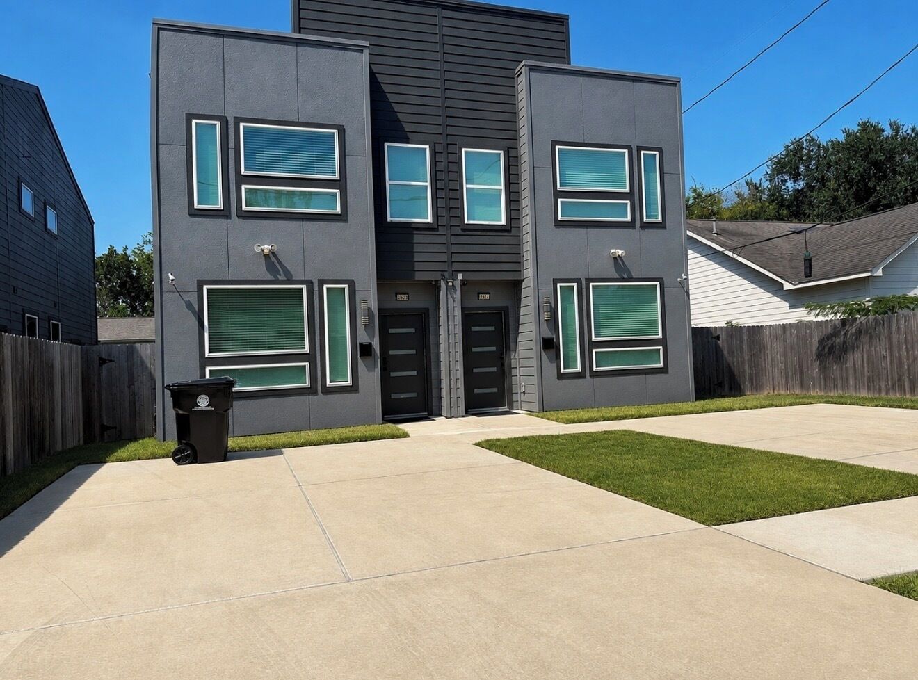 A modern two-story house with a garage, a front yard, and a trash bin.