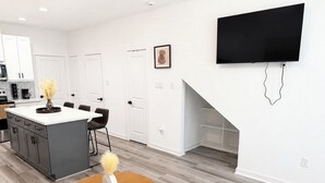 Eine moderne Küche mit weißen Schränken, ein Essbereich mit einem runden Tisch und ein an der Wand montierter Flachbildfernseher.