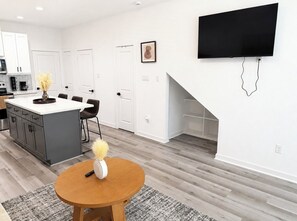 A modern kitchen with white cabinets, a dining area with a round table, and a flat-screen TV mounted on the wall. - H-Town Dream Deluxe Stay (Houston)