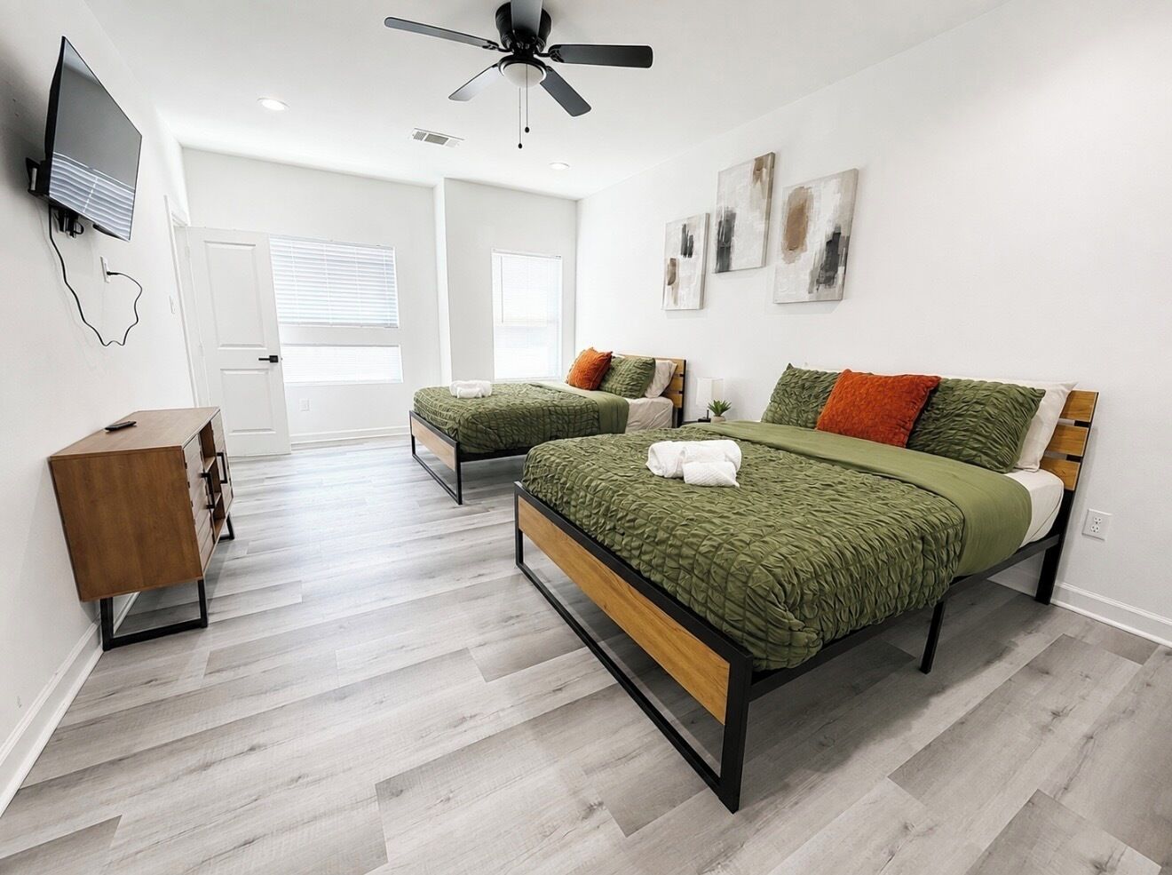 A bedroom with two beds, a ceiling fan, a TV, and a wooden dresser.