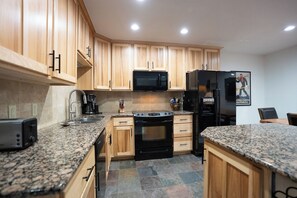 A kitchen with wooden cabinets, a black microwave, a black refrigerator, a stove, and granite countertops. - Ski Hill Powder Retreat: Downtown Breck, Walk to Gondola (Breckenridge)