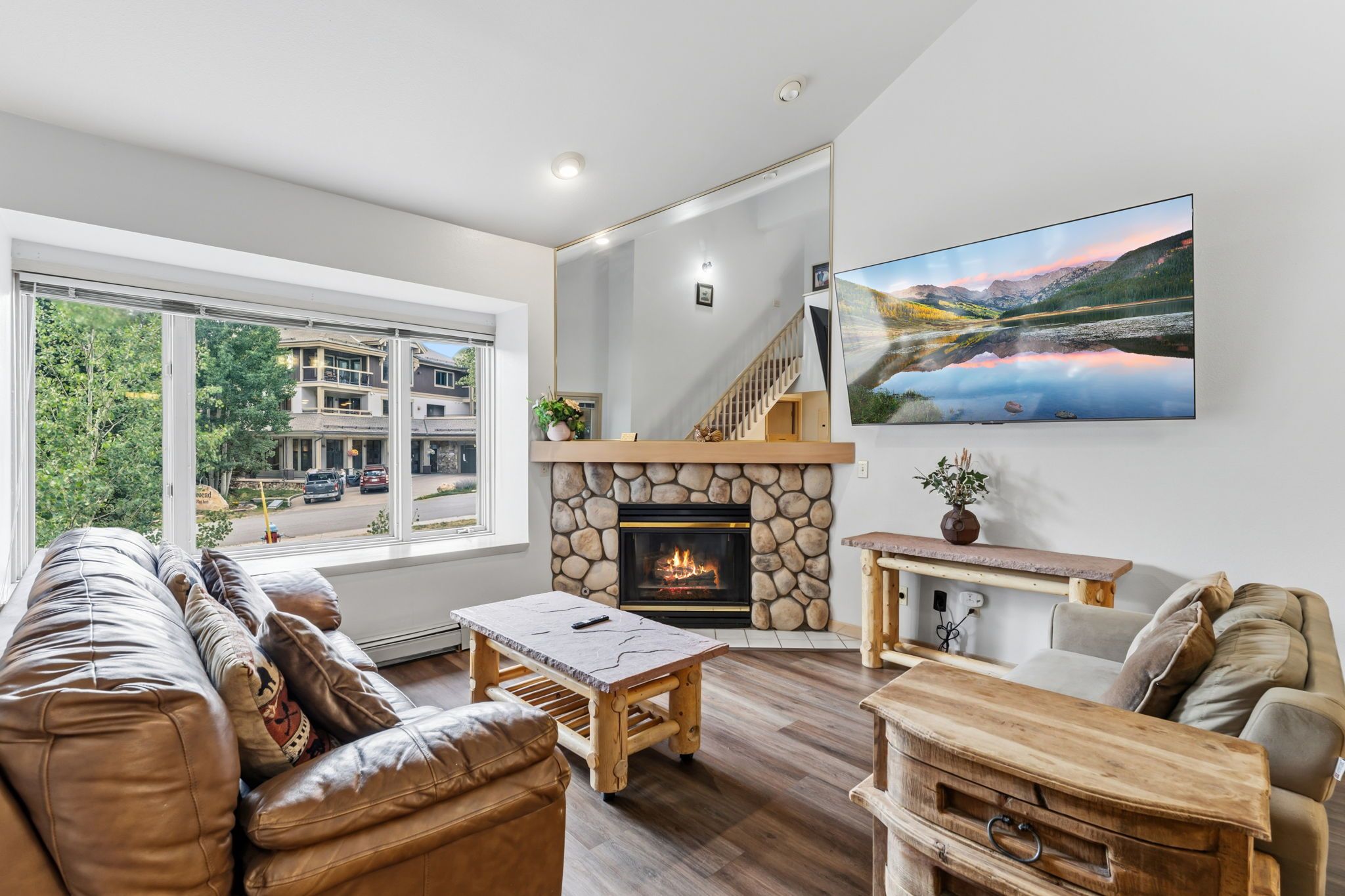 Una sala moderna con chimenea de piedra, sofá de cuero, mesa de centro de madera y un televisor de pantalla plana grande montado en la pared.
