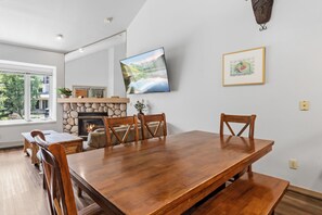 Ein Essbereich mit Holztisch und Stühlen, einem Kamin, einem an der Wand montierten Fernseher und einem gerahmten Bild.
