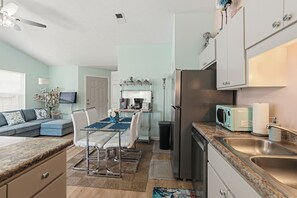 Eine moderne Küche mit Kühlschrank, Mikrowelle und Spüle. Es gibt eine Essecke mit Tisch und Stühlen.