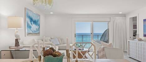 Un salon moderne avec vue sur la mer, un coin repas avec une table dressée pour quatre personnes et un balcon doté d’une balustrade.