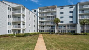 A multi-story residential building with balconies, a central pathway, and well-maintained lawns. - 2BR Beachfront 30A Condo | Private Beach, Pool & Tennis (Seacrest)