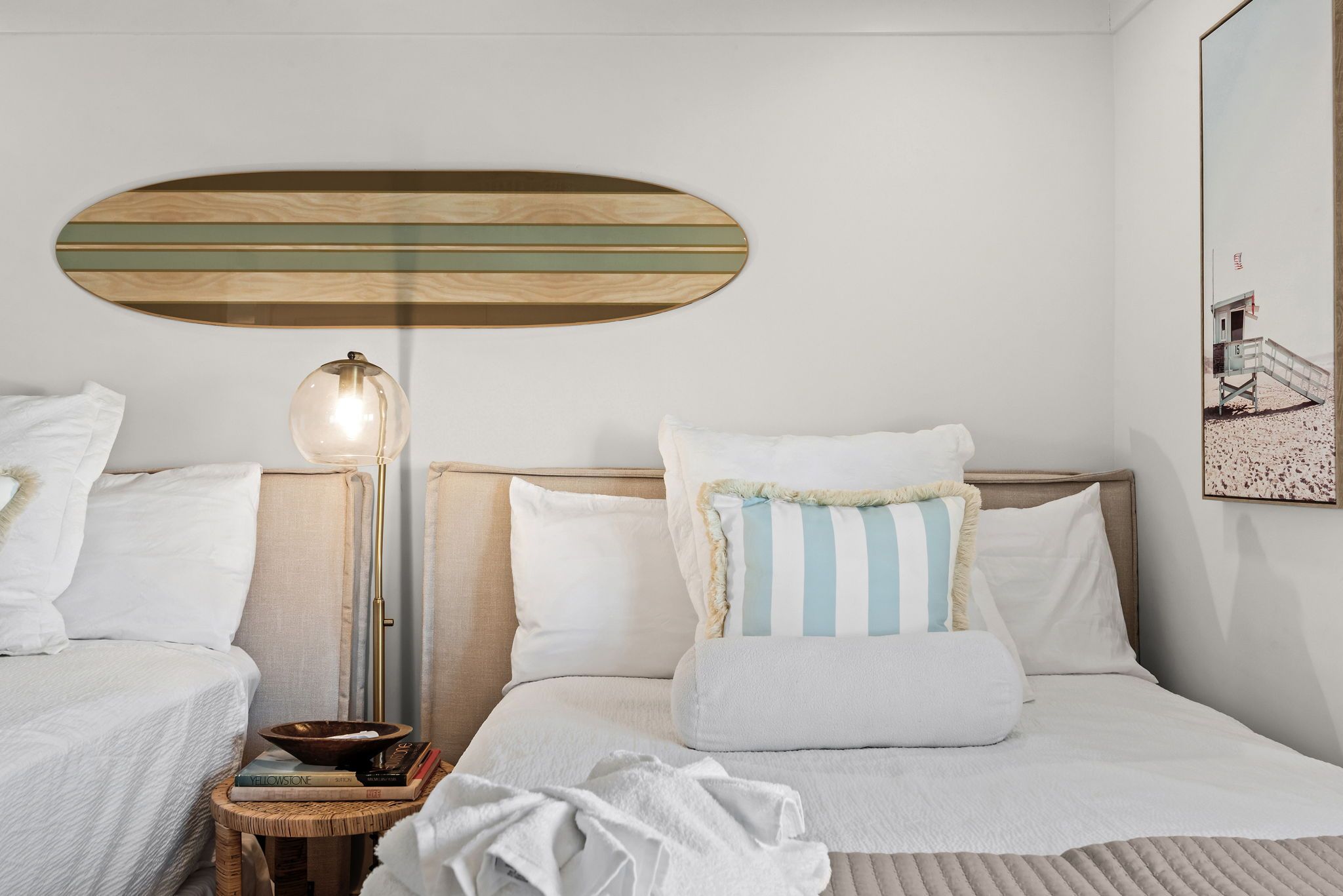 A hotel room with two beds, a bedside table with a lamp, and a wall-mounted artwork.