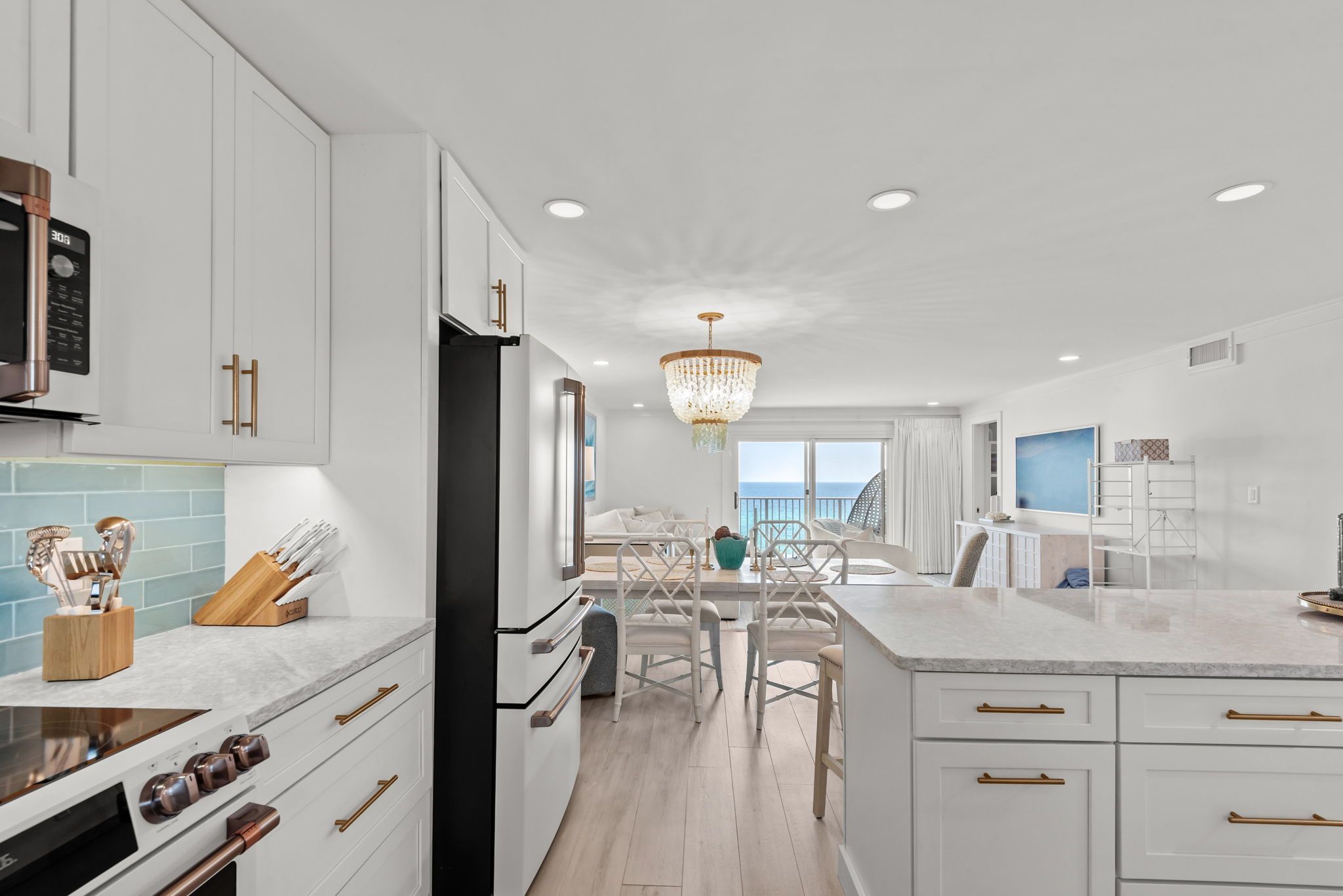 A modern kitchen with white cabinetry, a central island, and a view to the sea.
