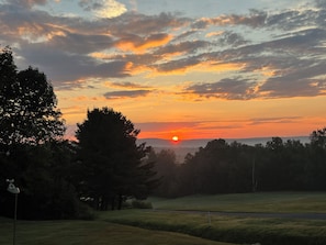 Ein Sonnenuntergang über einer grünen Landschaft mit Bäumen und klarem Himmel.