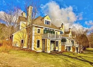 Une grande maison à deux étages, dotée d’une cheminée imposante, d’un balcon et d’une pelouse bien entretenue.