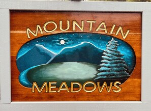 A framed artwork with the text 'MOUNTAIN MEADOWS' and a depiction of mountains, a tree, and a moon. - Warm and inviting condo 5 mins to Mt Snow-Dog friendly, 2 fireplaces, Great wifi (Wilmington)