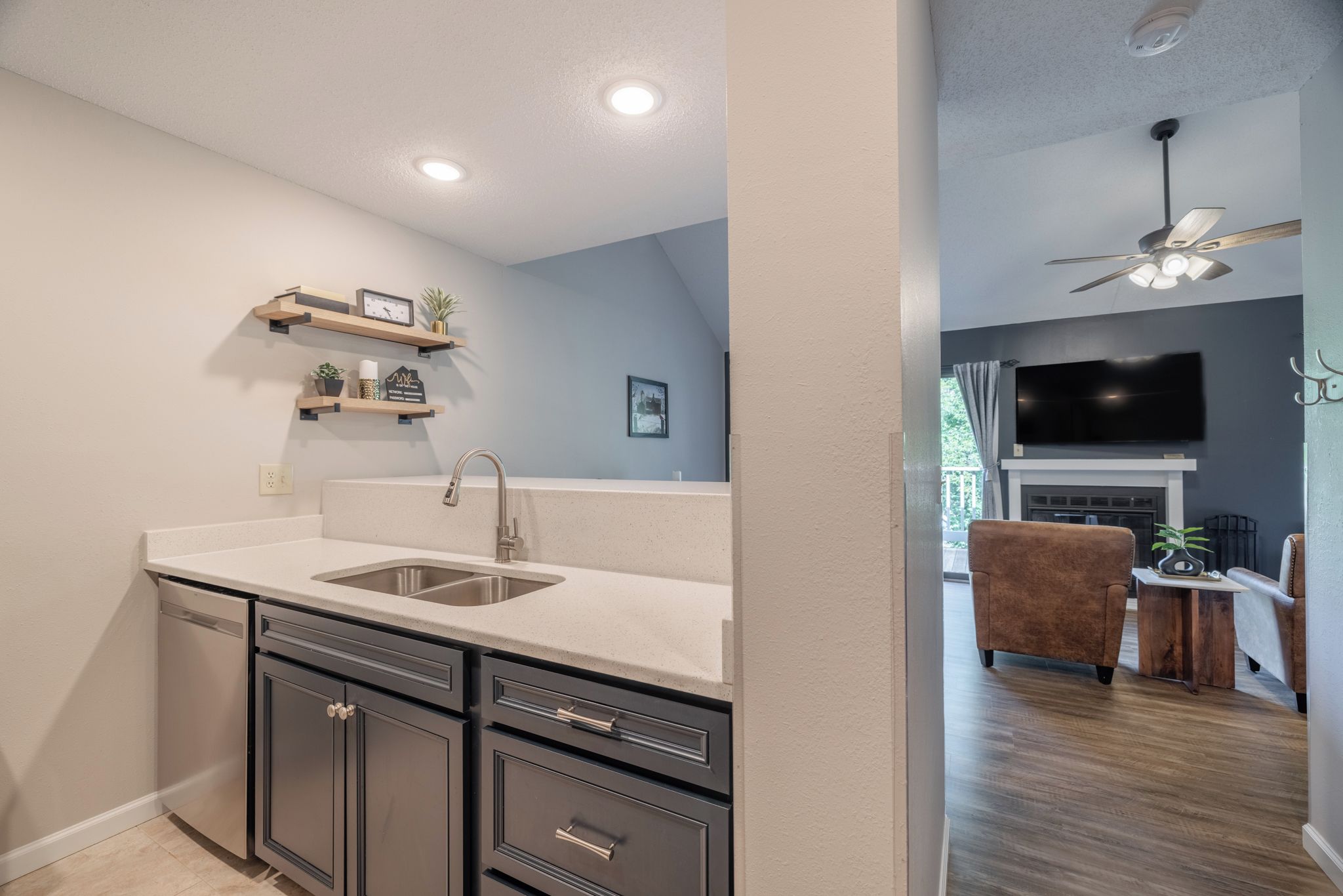A modern kitchen with a sink, cabinets, and a countertop. There is a dining area with a couch and a TV.