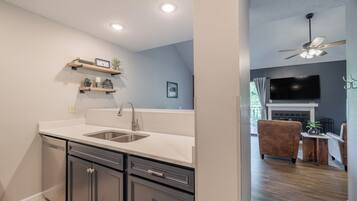 A modern kitchen with a sink, cabinets, and a countertop. There is a dining area with a couch and a TV.