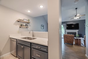 A modern kitchen with a sink, cabinets, and a countertop. There is a dining area with a couch and a TV. - Lake Aspen Getaway by Innsbrook Vacations! (Innsbrook)