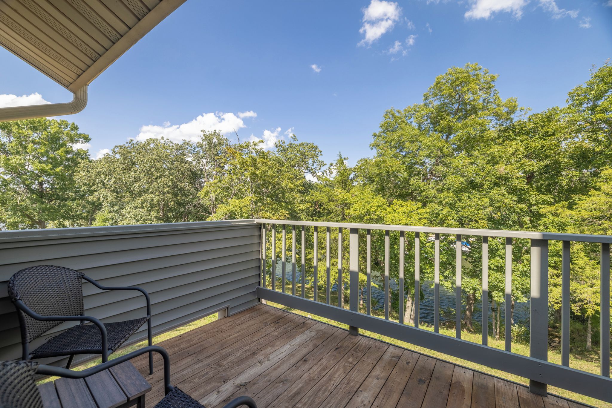 A wooden deck with a metal railing, a chair, and a view of a lake surrounded by trees.