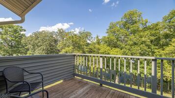 A wooden deck with a metal railing, a chair, and a view of a lake surrounded by trees.
