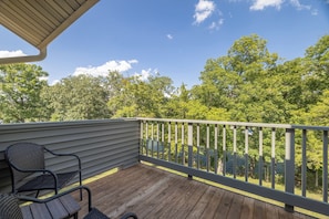 A wooden deck with a metal railing, a chair, and a view of a lake surrounded by trees. - Lake Aspen Getaway by Innsbrook Vacations! (Innsbrook)