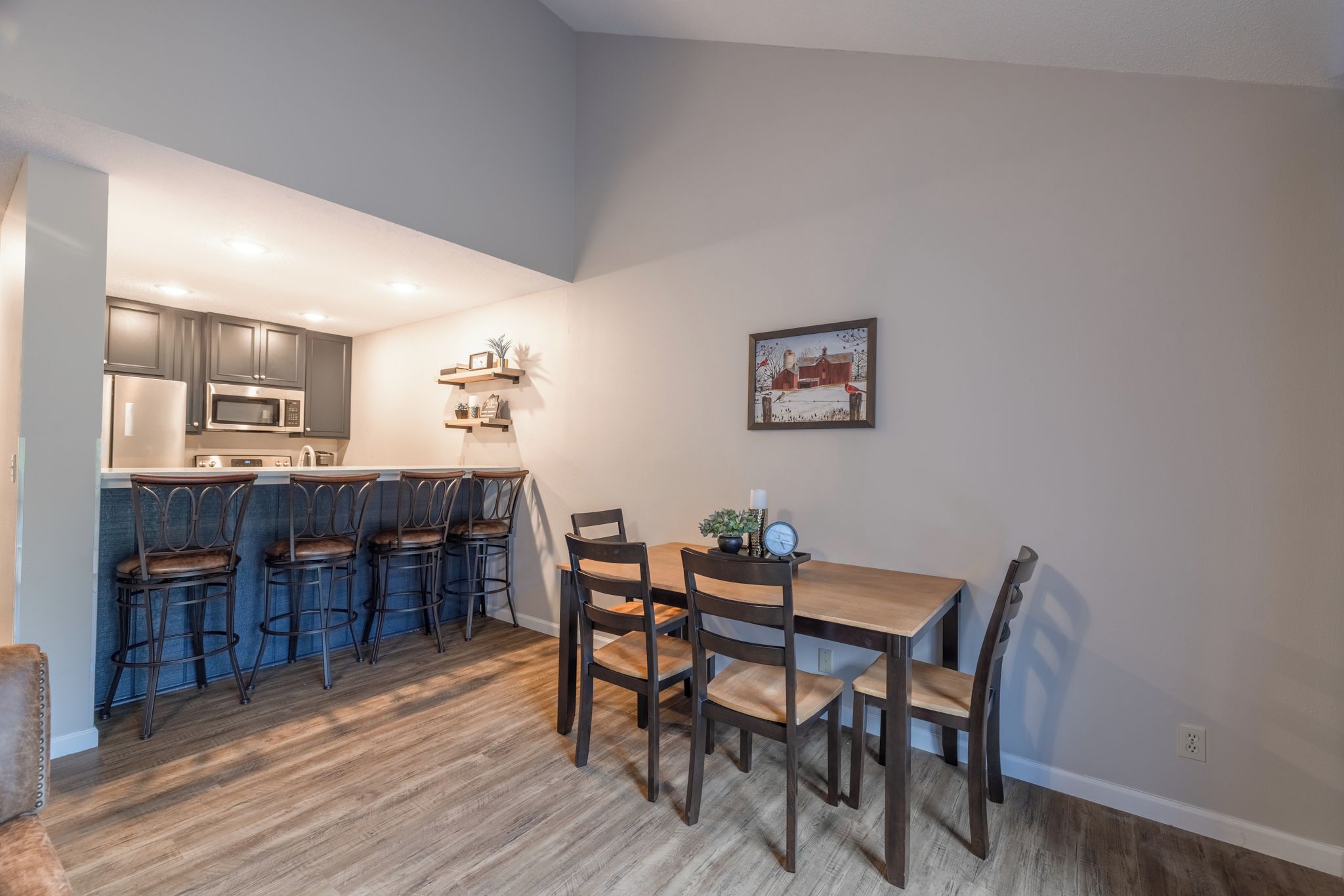 A compact kitchen with a bar area, wooden flooring, and a dining table with chairs.