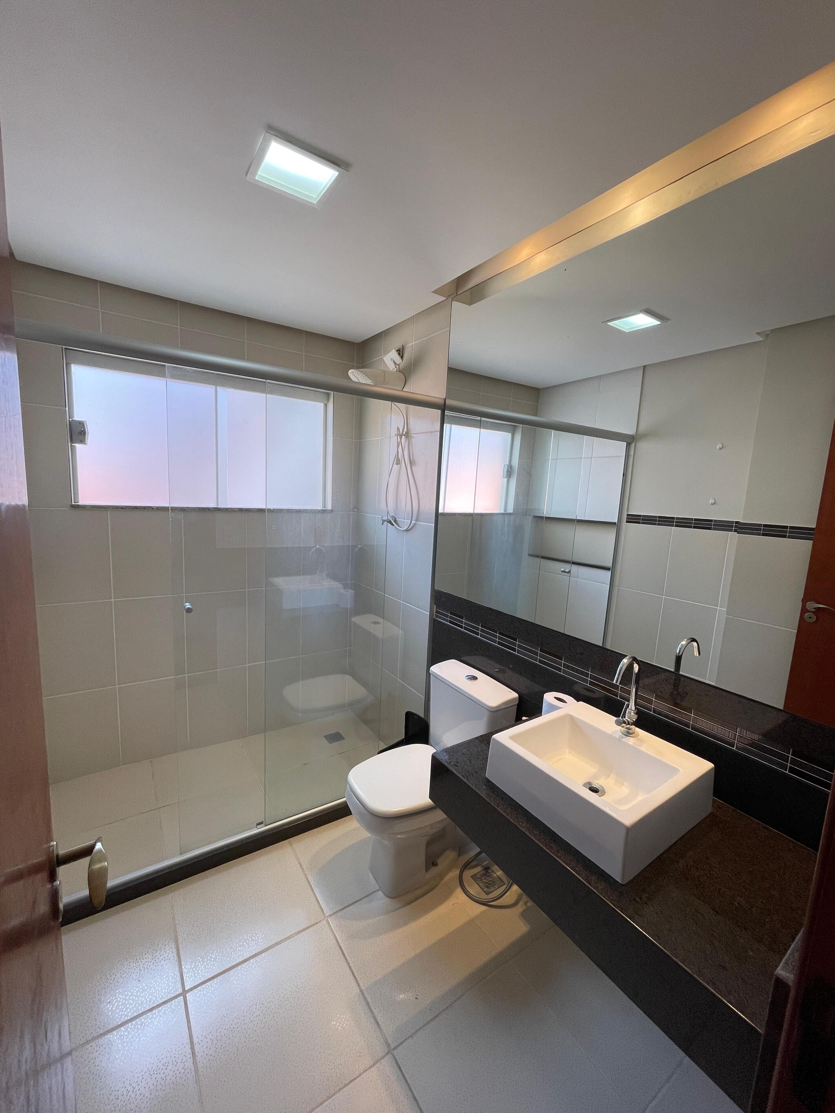 Une salle de bain moderne avec une douche à parois de verre, des toilettes blanches et un double lavabo doté d’un plan de travail noir.