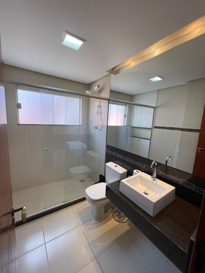 Een moderne badkamer met een douchecabine van glas, een wit toilet en een wastafel met dubbele spoelbak en een zwart aanrecht.