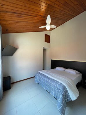 Een slaapkamer met een bed, een plafondventilator, een klein plankje en een raam.