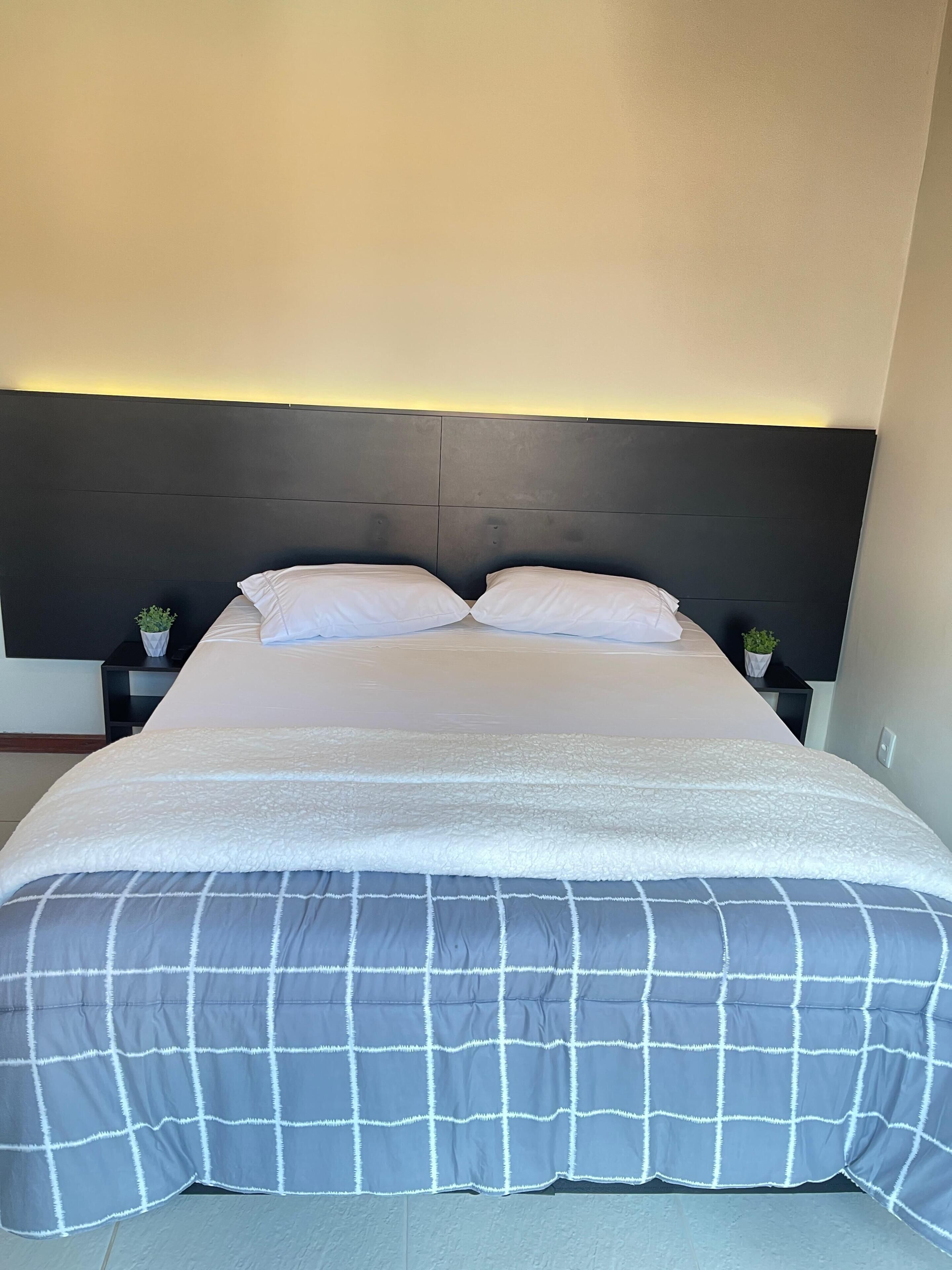 Un lit avec une tête de lit sombre, des oreillers blancs et une couvre-lit à carreaux gris et blancs.