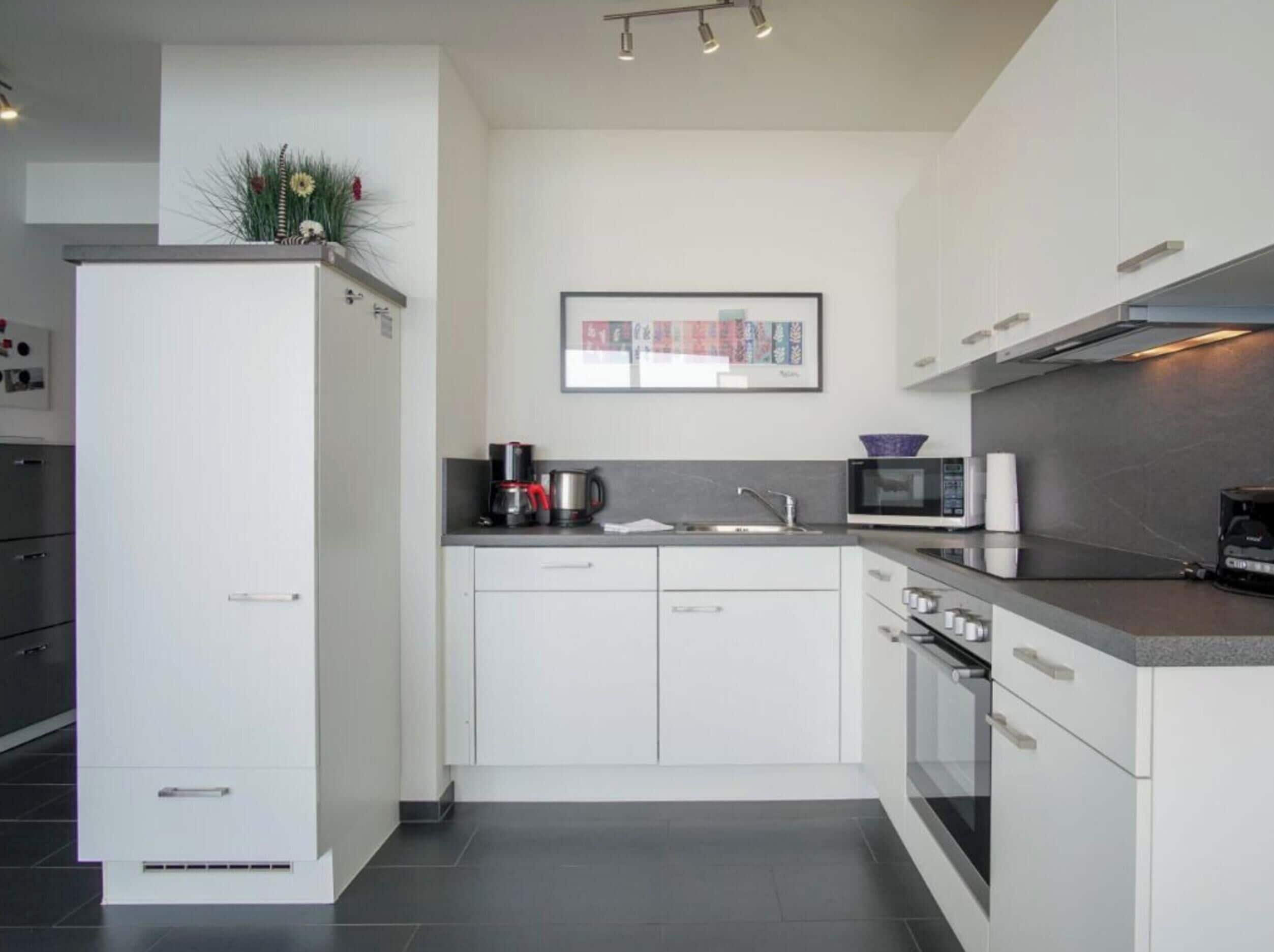 Una cocina moderna con armarios blancos, horno empotrado, microondas y cafetera.