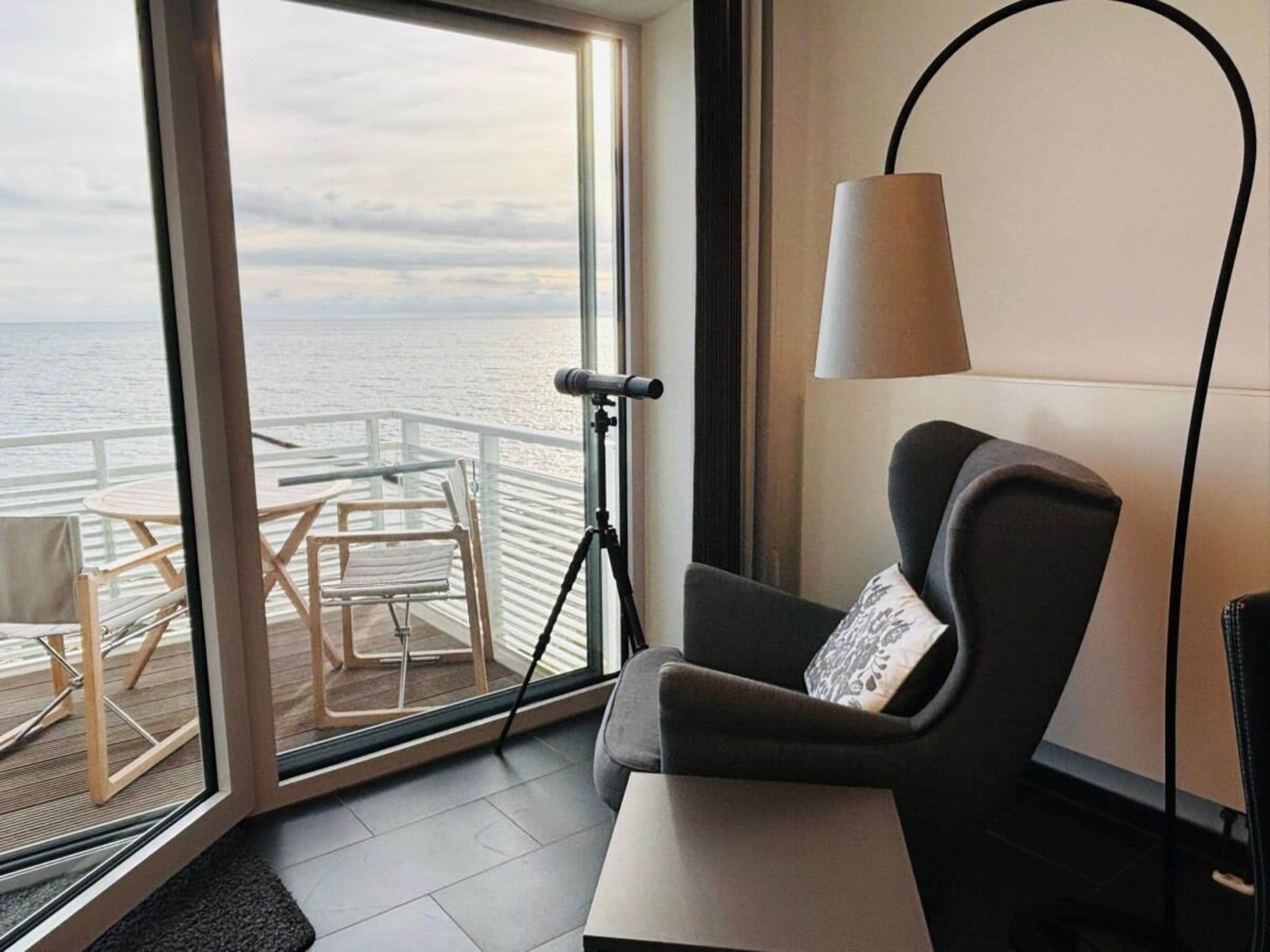 Ein Zimmer mit Meerblick, einem Stativ, einer Lampe und einem Sessel mit Kissen.
