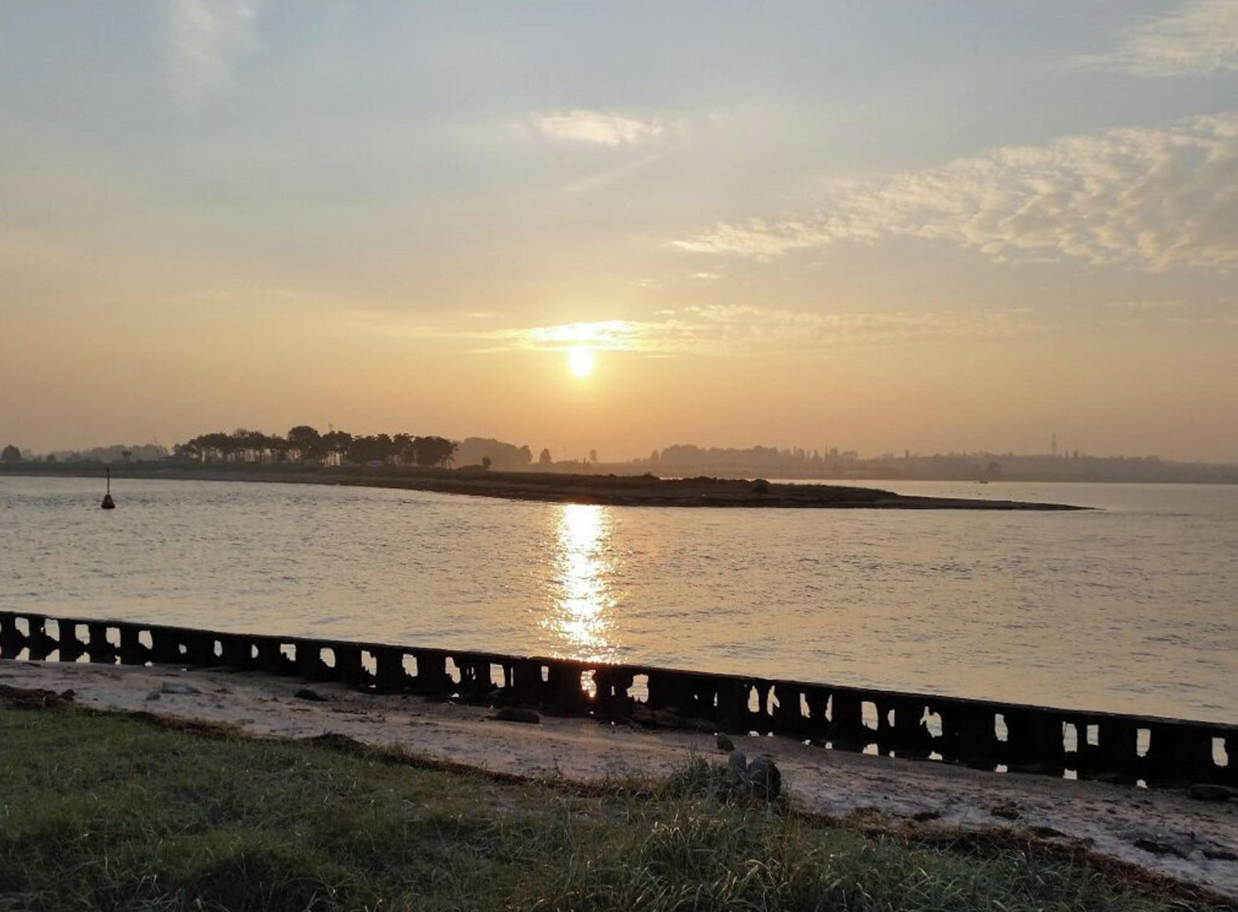 Solnedgang over vand med en fjer fjerne kystlinje og en bro i forgrunden.