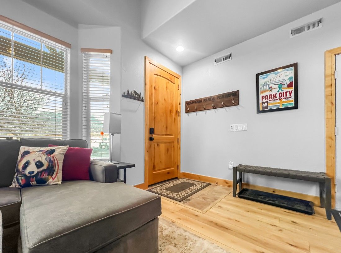A room with a sofa, a wooden door, a wall-mounted coat rack, and a poster.