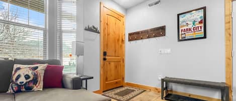 Una habitación con un sofá, una puerta de madera, un perchero en la pared y un cartel.