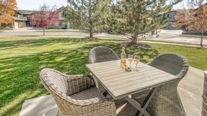 An outdoor patio with wicker furniture and a table, surrounded by a well-maintained lawn and trees. - Mountain Panda Paradise, 2BR Redstone Townhome, Close to Canyons (Park City)