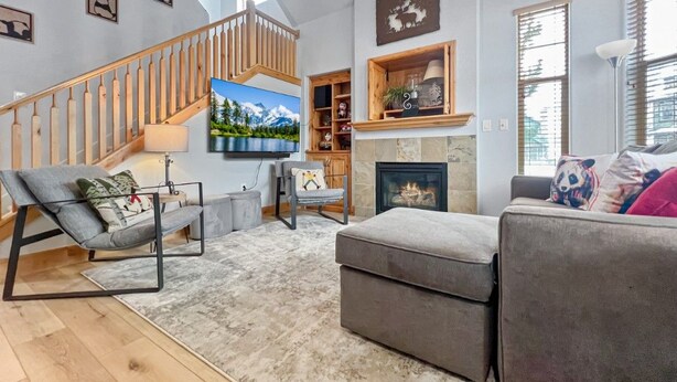 A modern living room with a staircase, a fireplace, and a large window. - Mountain Panda Paradise, 2BR Redstone Townhome, Close to Canyons (Park City)
